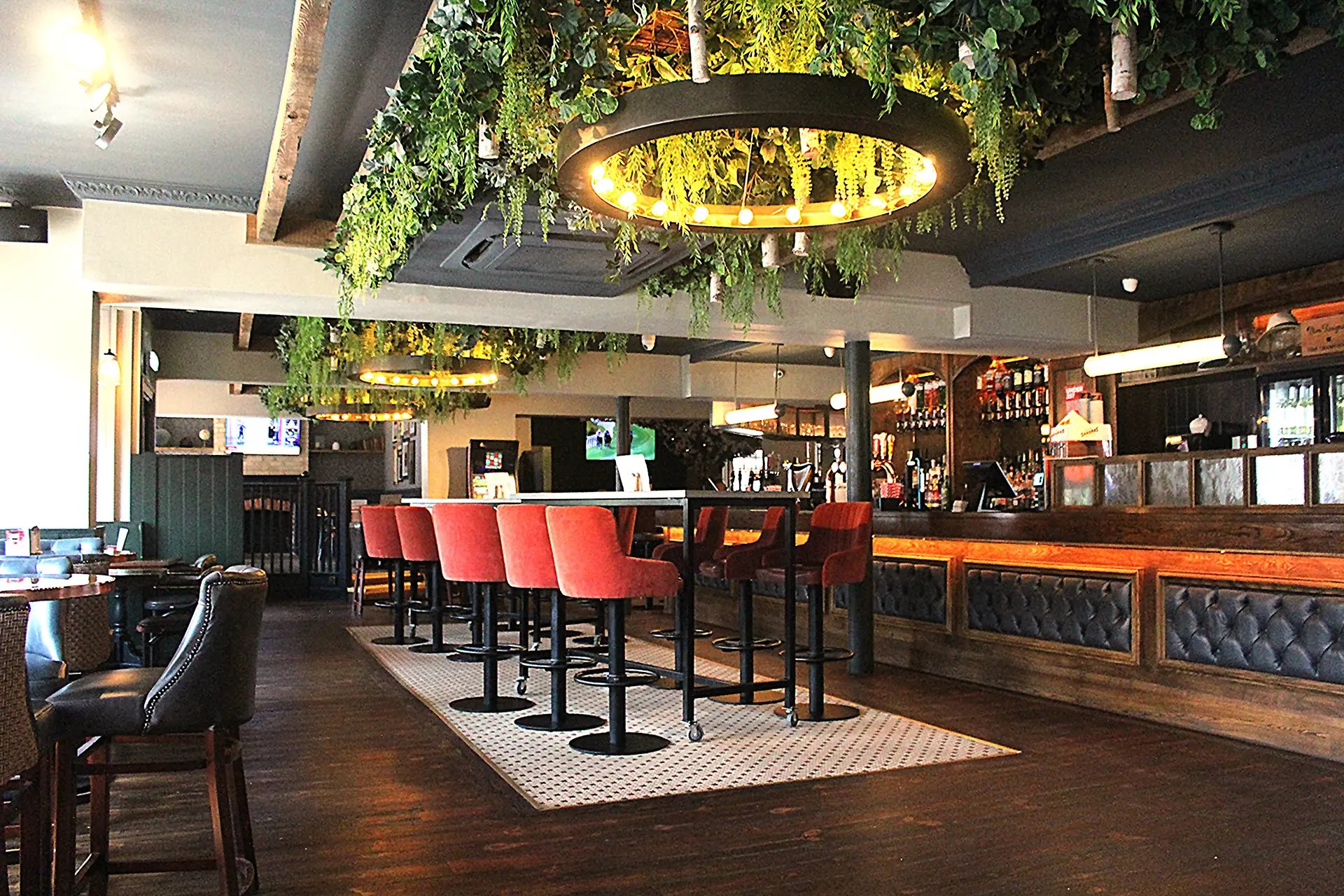 The bar at The Foundry, hanging greenery overhead and red stools in front
