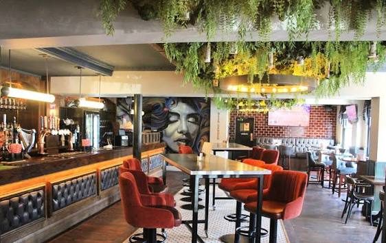 Inside The Foundry: red velvet chairs and booths under hanging greenery, with a painted mural on the brick wall