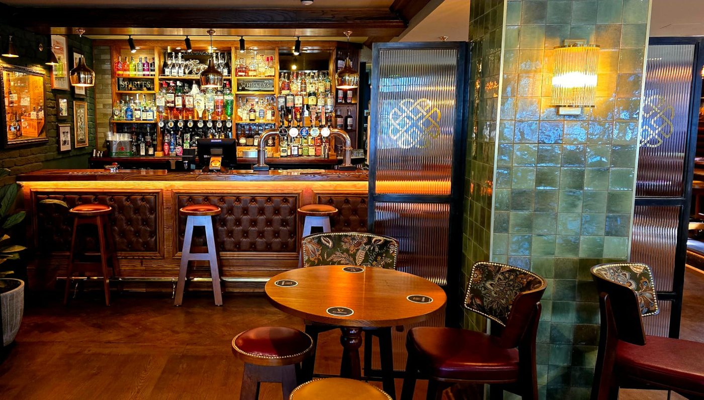 The bar at Whelan's Uxbridge: stools along the counter, green tiles and a backlit wall of spirits