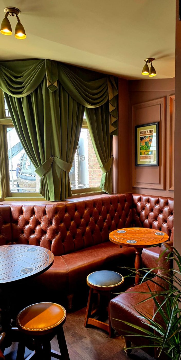 A leather banquette in a bay window, framed by heavy green curtains